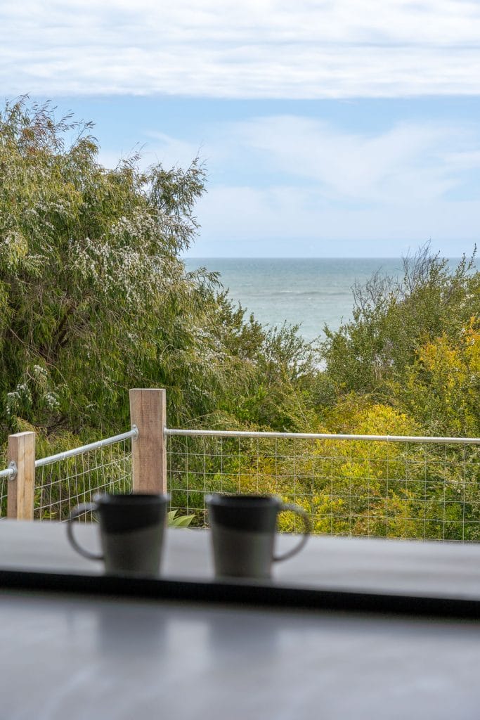 Photo of two coffee mugs on the windowsill with trees and sea in the background