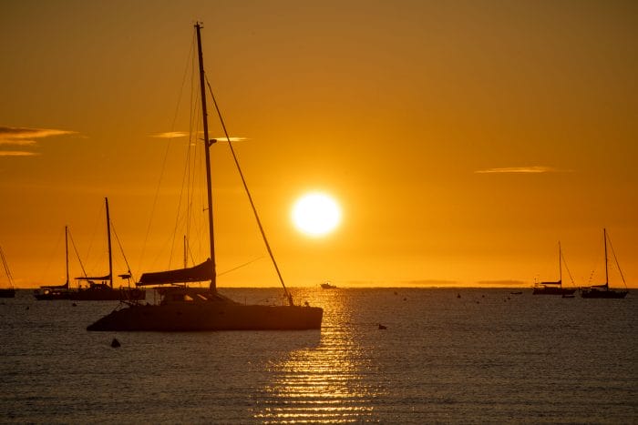 Photo of the sun setting behind a sailing boat